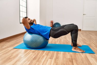 Yakışıklı İspanyol adam egzersiz yapıyor ve yoga minderinde geriniyor, spor salonunda pilates topuyla esneklik gösteriyor.