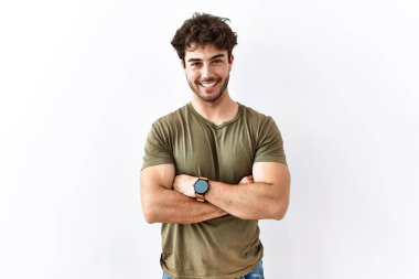 İzole edilmiş beyaz arka planda duran İspanyol adam kollarını kavuşturup kameraya bakarken gülümsüyor. pozitif kişi. 