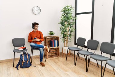 Genç İspanyol adam, bekleme odasında müzik dinlerken kendinden emin bir şekilde gülümsüyor.