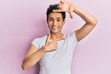 Gündelik beyaz tişört giyen, gülümseyen, elleri ve parmakları gülen yüzlü genç yakışıklı bir adam. yaratıcılık ve fotoğrafçılık kavramı. 