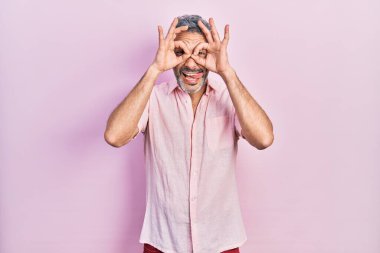 Gri tişörtlü, yakışıklı, orta yaşlı bir adam. Dürbün gibi güzel hareketler yapıyor. Gözleri parmaklarından bakıyor. çılgın ifade. 