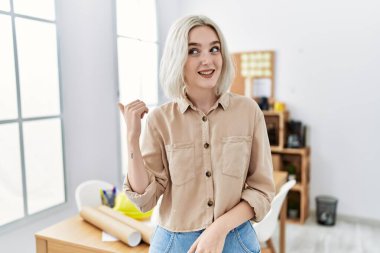 İnşaat ofisindeki genç, güzel beyaz kadın gülen yüzle gülümsüyor ve başparmağıyla yan tarafı işaret ediyor.. 