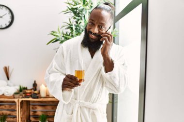 Genç Afro-Amerikalı adam akıllı telefondan konuşuyor güzellik merkezinde şampanya içiyor.