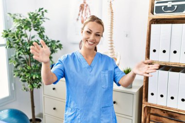 Ağrı kesici kliniğinde çalışan beyaz bir kadın kameraya sarılıp gülümsüyor. Mutluluğu kucaklayan neşeli bir ifade.. 