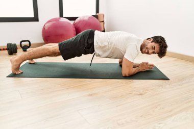 Genç İspanyol adam gülümsüyor spor merkezinde kendine güvenen karın kasları egzersizi yapıyor.