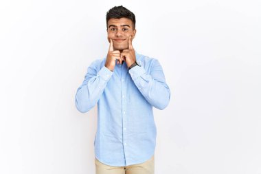 İzole edilmiş arka planda duran İspanyol gömlekli genç adam ağzı açık gülümsüyor, parmakları işaret ediyor ve neşeli bir gülümseme sergiliyor. 