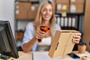 Genç sarışın kadın ecommerce iş çalışanı ofiste barkod okuyucu kullanarak paket tarama