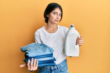 Çamaşır yıkayan beyaz bir kadın elinde deterjan şişesi ve katlanmış kot pantolon tutarken yüzünde ciddi bir ifadeyle rahatlıyor. Basit ve doğal bir şekilde kameraya bakıyorsun.. 