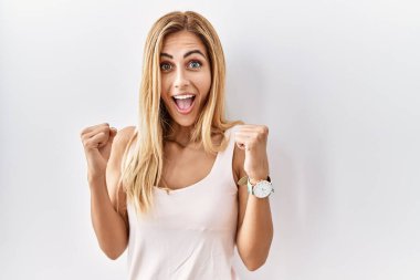 Sarışın, güzel, izole edilmiş beyaz arka planda duran genç bir kadın kollarını kaldırarak ve açık gözlerle başarının şaşkınlığını ve şaşkınlığını kutluyor. Kazanan konsept. 