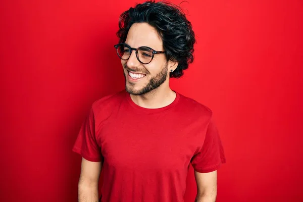 ハンサムなヒスパニック系の男性がカジュアルなTシャツや眼鏡を離れて顔に笑顔で横に見て 自然な表情を着て 自信を持って — ストック写真