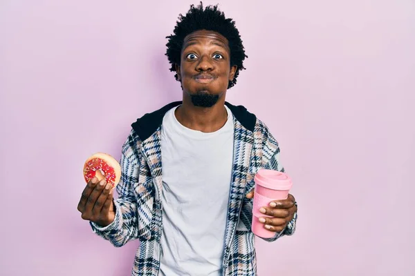 年轻的非洲裔美国人吃甜甜圈 喝着咖啡 脸上带着滑稽的表情 嘴被空气吹胀 — 图库照片
