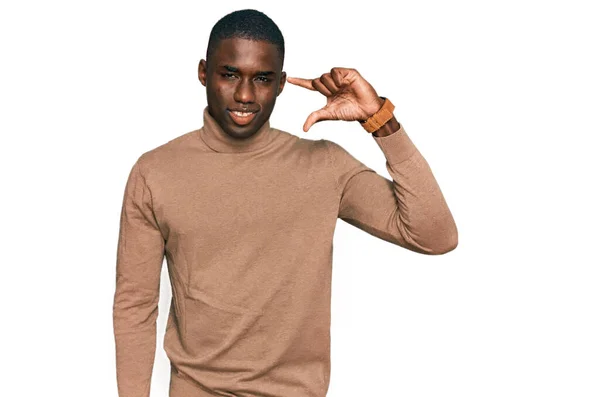 カジュアルな冬のセーターを着た若いアフリカ系アメリカ人男性が笑顔で 指を見てカメラで小さなサイズのサインをして手で自信を持ってジェスチャー 概念を測定し — ストック写真