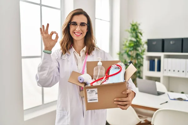 Young Doctor Woman Holding Box Medical Items Doing Sign Fingers — стоковое фото