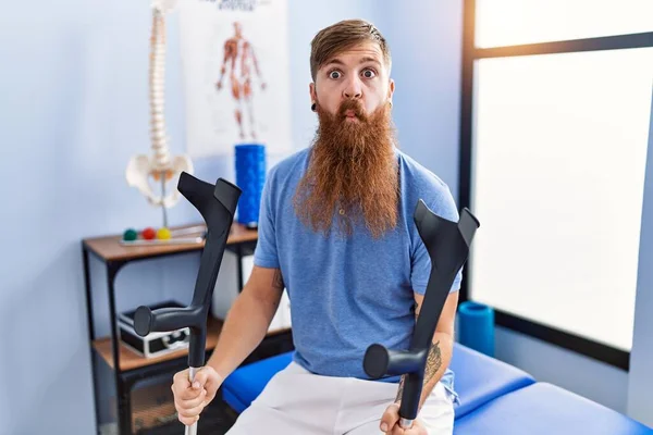 Redhead Man Long Beard Holding Crutches Rehabilitation Clinic Making Fish — стоковое фото