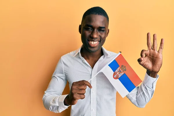 Joven Hombre Afroamericano Sosteniendo Bandera Serbia Haciendo Signo Con Los —  Fotos de Stock