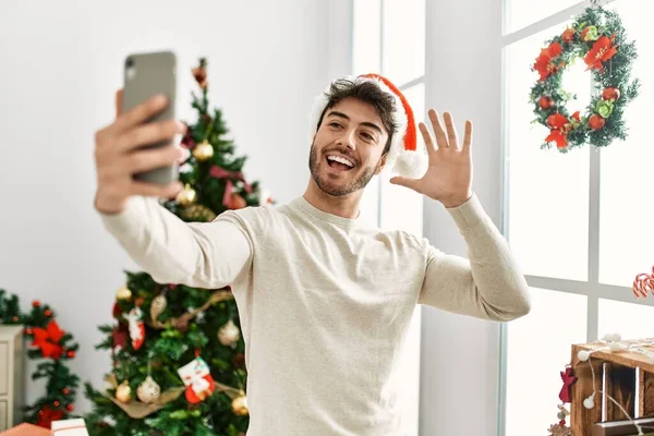 Young Hispanic Man Wearing Christmas Hat Making Selfie Smartphone Home — стоковое фото