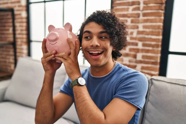 Young Hispanic Man Holding Piggy Bank Sitting Sofa Home — Zdjęcie stockowe