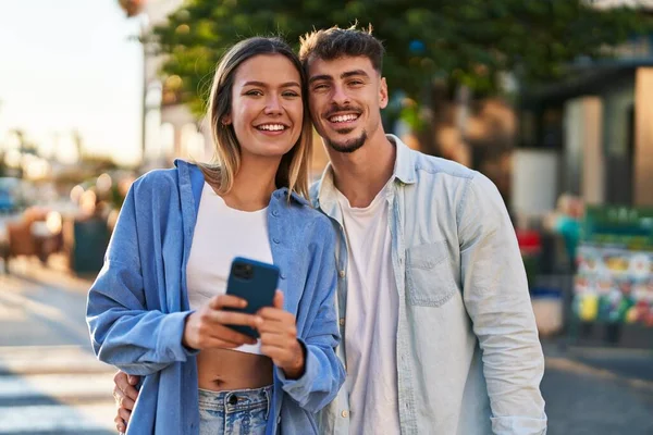 若い男と女のカップル笑顔自信を持って使用してスマートフォンでストリート — ストック写真