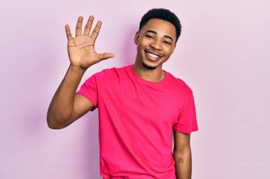 Casua tişörtü giyen genç Afro-Amerikan adam gülümseyen, kendinden emin ve mutlu beş numarayı gösteriyor ve işaret ediyor.. 