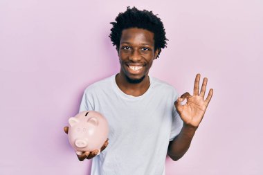 Genç Afrikalı Amerikalı domuz kumbarası tutuyor. Parmaklarıyla imza atıyor, gülümsüyor. Mükemmel bir sembol. 