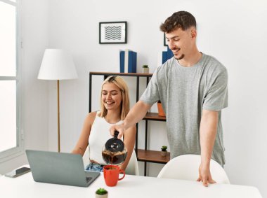 Kadın evde dizüstü bilgisayar kullanıyor ve erkek arkadaşı kahve dolduruyor..