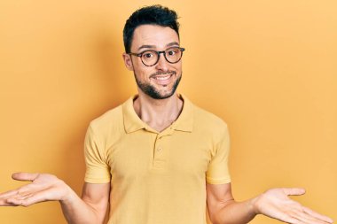 Sıradan kıyafetler giyen, gözlüklü, kafası karışık, elleri ve kolları havada bir İspanyol. şüphe kavramı. 