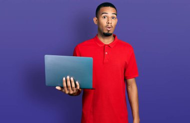 Genç Afro-Amerikan bir adam bilgisayar laptopuyla çalışıyor. Şaşırtıcı bir şekilde korkmuş ve hayrete düşmüştü. İnanmayan yüz. 