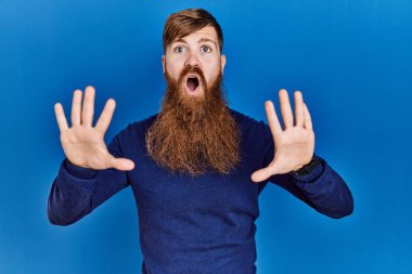 Uzun sakallı kızıl saçlı adam mavi arka planda günlük mavi süveter giyiyor. Avuç içi hareketlerini durduruyor. Öfkeli ve hayal kırıklığı dolu bir ifade takınıyor. 