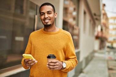 Genç Afrikalı Amerikalı adam akıllı telefon kullanıyor. Şehirde kahve içiyor..