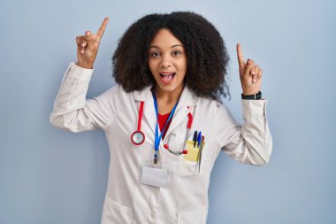 Genç Afro-Amerikan kadın doktor üniforması ve steteskop giymiş şaşkın şaşkın gülüyor, parmaklarıyla işaret ediyor ve kollarını kaldırıyordu.. 