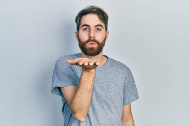 Beyaz sakallı, sıradan gri tişörtlü bir adam kameraya bakıp havada bir öpücük savuruyor. Güzel ve seksi. aşk ifadesi. 