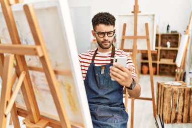 Sanat stüdyosunda akıllı telefon çizimi yapan genç bir Arap sanatçı..