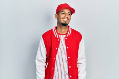 Beyzbol üniforması giyen genç Afro-Amerikan adam yüzünde gülümseme, doğal bir ifade ile yan yana bakıyor. Kendinden emin gülen. 