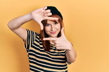 Kızıl saçlı, yün şapka takan, gülümseyen, elleri ve parmakları gülen yüzlü bir kadın. yaratıcılık ve fotoğrafçılık kavramı. 