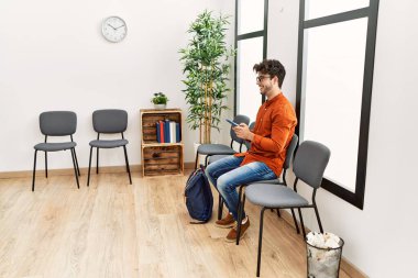 Young hispanic man smiling confident using smartphone at waiting room