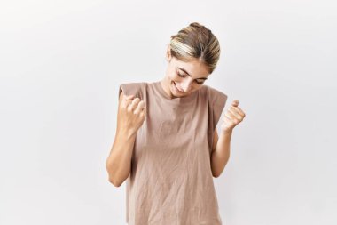 Soyutlanmış arka planda duran genç sarışın kadın mutlu ve heyecanlı bir şekilde kollarını kaldırıp, gülümseyip, başarı için haykırıyor. kutlama konsepti. 