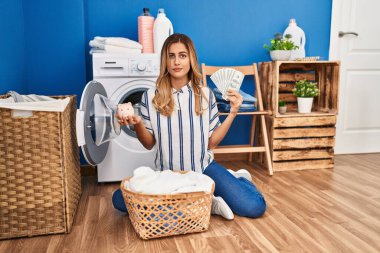 Çamaşır yıkayan genç sarışın kadın para tasarrufu yapıyor şüpheci ve gergin, sorun yüzünden surat asıyor. negatif kişi. 