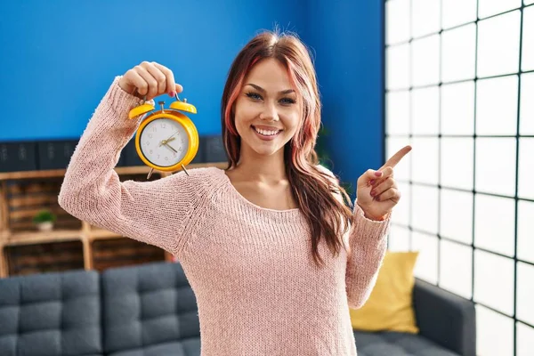 Young Caucasian Woman Holding Alarm Clock Smiling Happy Pointing Hand — Stock Photo, Image