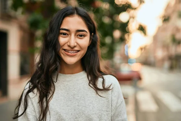 Genç ortadoğulu kız gülümsüyor, mutlu bir şekilde şehirde duruyor..