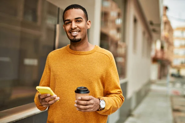 Genç Afrikalı Amerikalı adam akıllı telefon kullanıyor. Şehirde kahve içiyor..