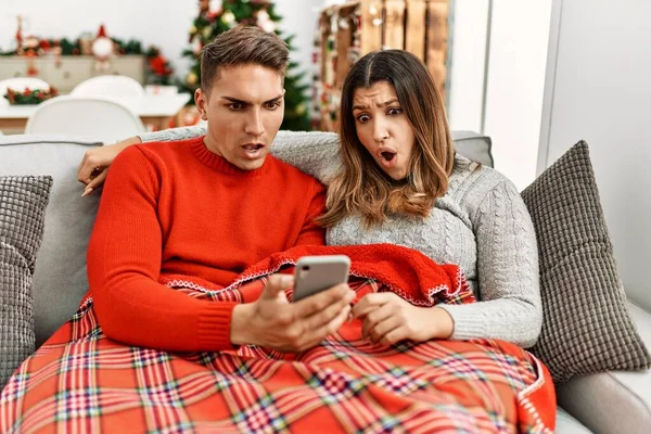 Young Hispanic Couple Sitting Sofa Christmas Scared Amazed Open Mouth — Stok fotoğraf