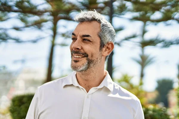 Orta yaşlı, kır saçlı, gülümseyen bir adam şehirde mutlu bir şekilde duruyor..