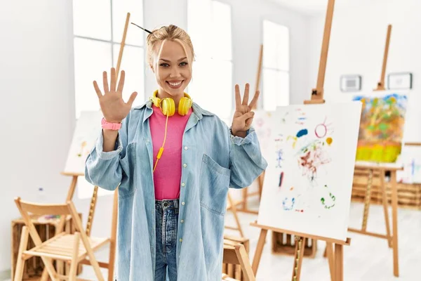 Young caucasian girl at art studio showing and pointing up with fingers number eight while smiling confident and happy.