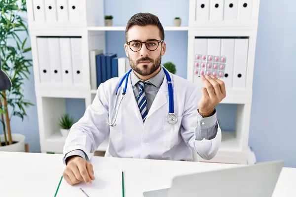 Handsome Hispanic Man Wearing Doctor Uniform Holding Prescription Pills Thinking — 스톡 사진