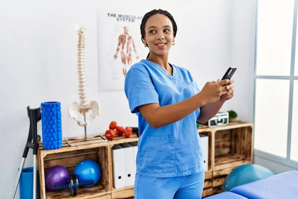 Young African American Woman Wearing Physio Therapist Uniform Using Smartphone — стоковое фото
