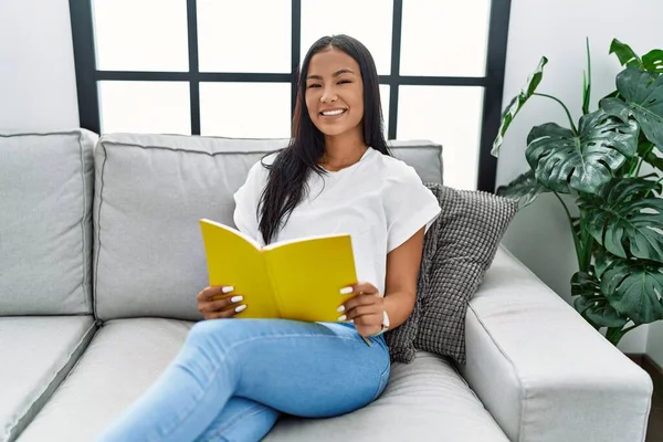 Genç Latin kadın gülümsüyor evde kendine güvenen kitap okuyor.