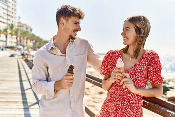 Genç İspanyol çift tatilde gülümseyerek kumsalda dondurma yiyor.