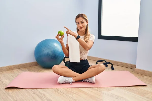 Young Blonde Woman Wearing Sportswear Towel Holding Healthy Apple Pointing — стоковое фото