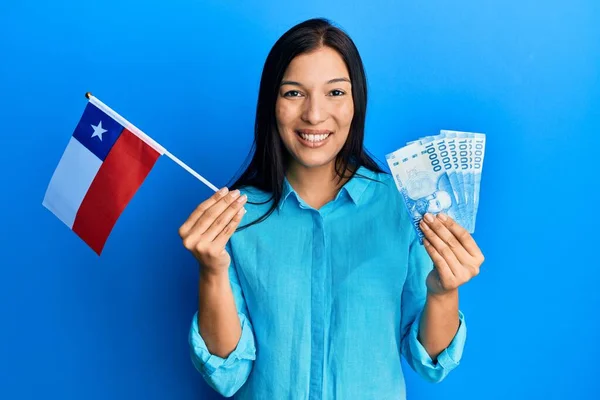 年轻的拉丁女子举着儿童国旗和儿童比索钞票 脸上挂着快乐而沉着的微笑 显示牙齿 — 图库照片