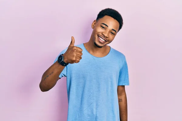 若いアフリカ系アメリカ人の男性が手で幸せな親指アップジェスチャーを行うカジュアルな青のTシャツを着ている 成功を示すカメラを見ると — ストック写真